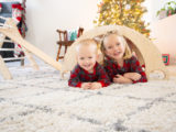 Two children peeking out from under a climbing arch amidst holiday decor. Captured by Charlie and Me Photography for brand marketing.