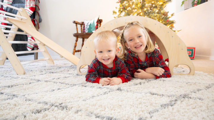 Two children peeking out from under a climbing arch amidst holiday decor. Captured by Charlie and Me Photography for brand marketing.