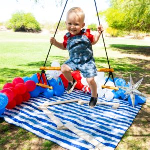 Child in overalls and red t-shirt joyfully swings, surrounded by red, white, and blue balloons – a playful and patriotic moment with Wiwiurka's toys